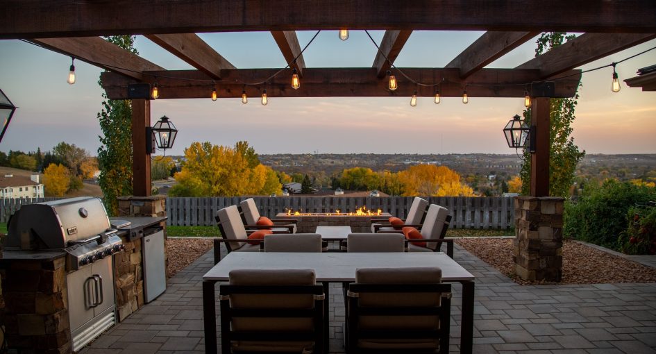 Outdoor patio seating under a pergola with a fire pit and grill